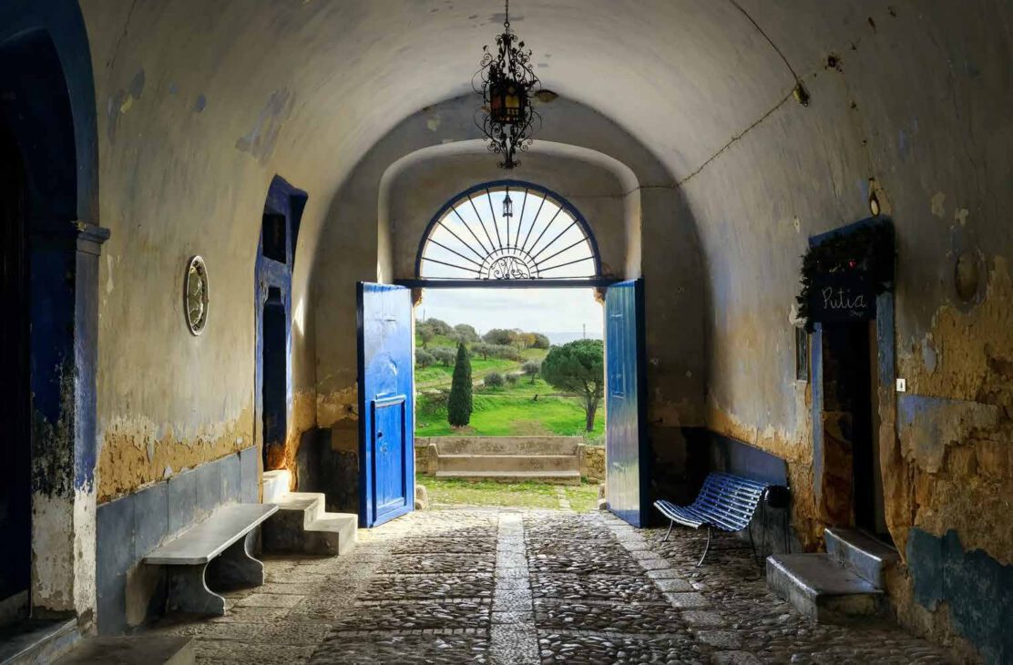 Historischer Torbogen mit blauen Türen und Blick ins Grüne